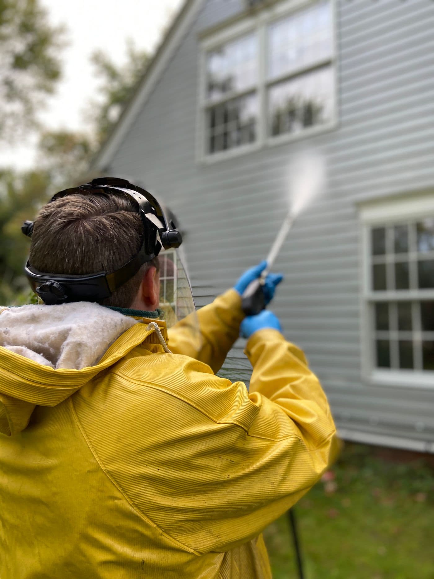 Pressure washing the exterior of a house in protective gear